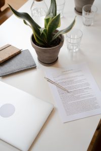 Bureau blanc avec un contrat posé à côté d'une plante verte et d'un ordinateur portable
