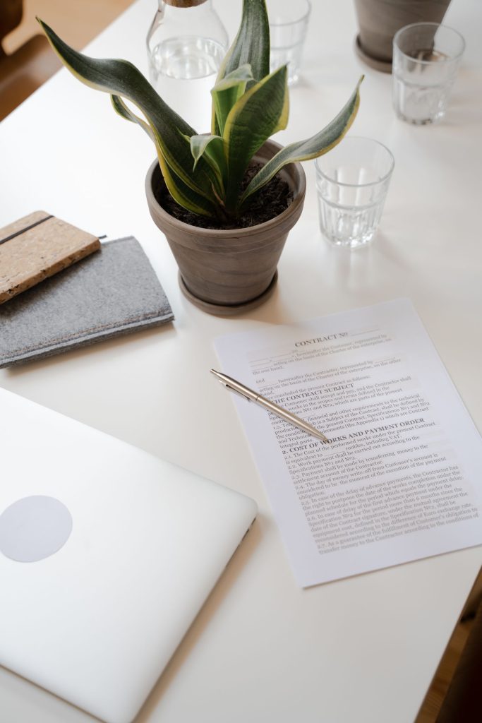 Bureau blanc avec un contrat posé à côté d'une plante verte et d'un ordinateur portable