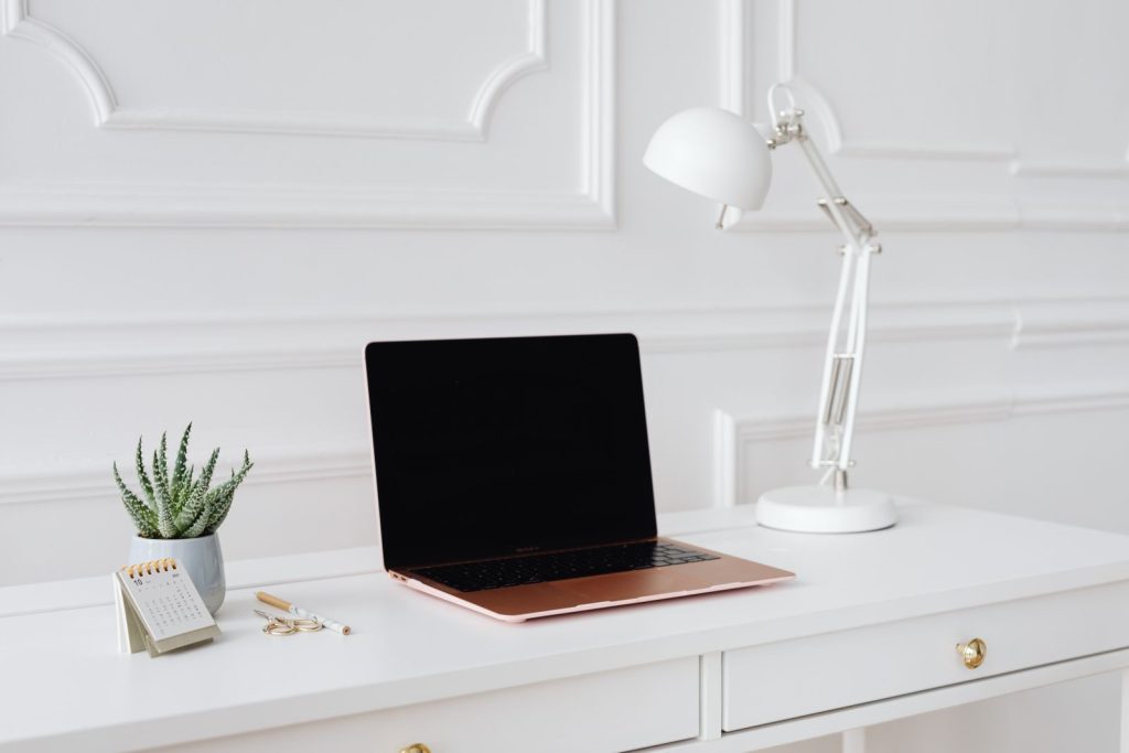 Bureau blanc avec un ordinateur portable, une lampe articulée et une plante